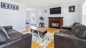 A living room with leather sofas, a wooden coffee table, a fireplace, and a flat-screen TV. - Spacious 4BR Home Sleeps 10 I Game Room + Sunroom+ Veranda (DIEPPE)