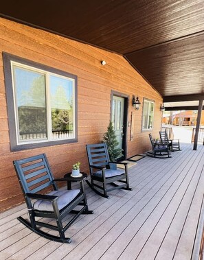 Ein Holzhaus mit einer überdachten Veranda, zwei Schaukelstühlen, einem kleinen Tisch mit einer Pflanze und einem Topfbaum.