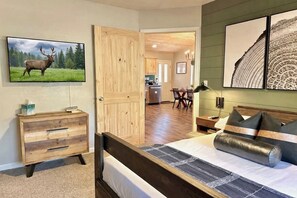 Ein Schlafzimmer mit einem Bett, einer hölzernen Kommode, einem Elchgemälde und Blick zur Küche.