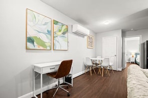 Ein modernes Wohnzimmer mit einem weißen Schreibtisch, einem braunen Sessel, einem Esstisch mit Stühlen und Bildern an den Wänden.