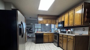 A kitchen with a refrigerator, stove, microwave, wooden cabinets, and a tiled floor. - Family and Pet Friendly Home in Benton, AR (Benton)