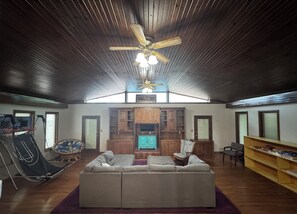 Un vaste espace de vie comprenant un grand canapé, des meubles en bois, un ventilateur de plafond et un téléviseur.