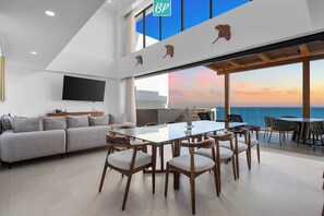A modern interior with a dining area, sofa, and large windows overlooking the sea. - Lux Beachfront 5BR Penthouse Retreat | Panarea (Bucerías)
