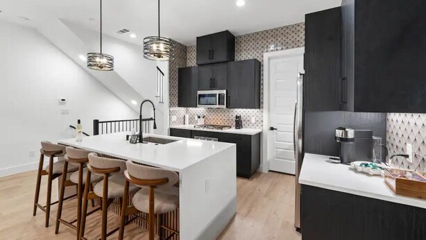Una cocina moderna con una isla central, taburetes de bar y un microondas.