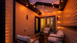 Un patio al aire libre con paredes de madera, luces colgantes y mobiliario blanco.