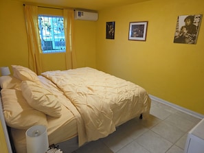Ein Zimmer mit einem Bett, einem Vorhangfenster, einer Klimaanlage und Bilderrahmen an der Wand.