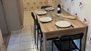 Ein Essbereich mit einem Holztisch, gedeckt für vier Personen, Stühlen, einer Weinflasche und einer Obstplatte.