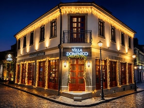 A building with a sign reading 'Villa Domenico' and 'Restaurant & Pizza.' It features a cobblestone street, a balcony with a railing, and multiple windows with string lights.