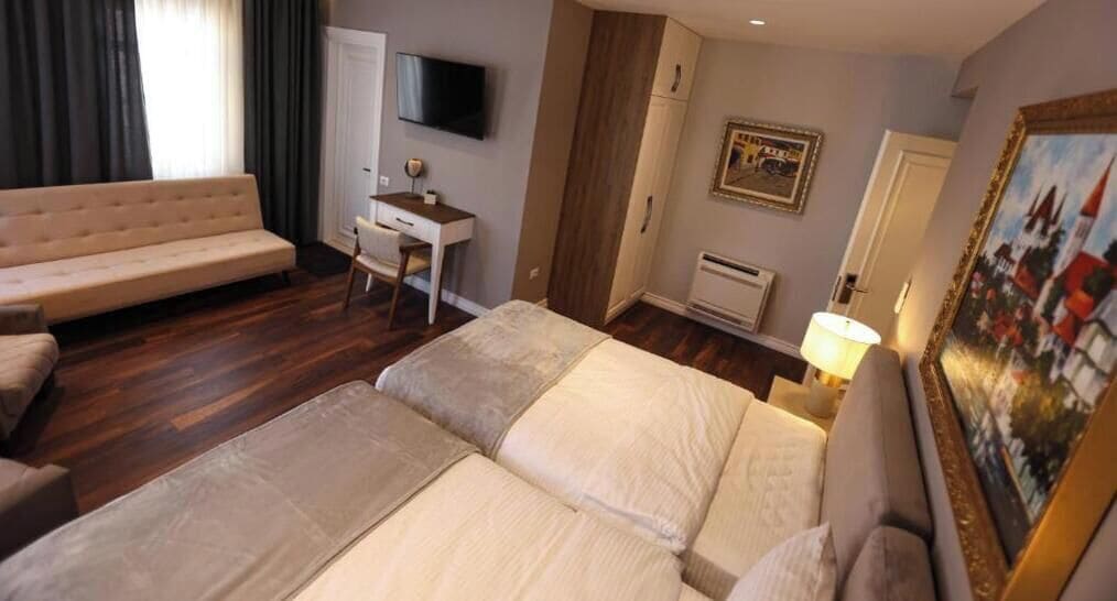 A hotel room with a bed, a sofa, a desk, a TV, a painting, and a wardrobe.