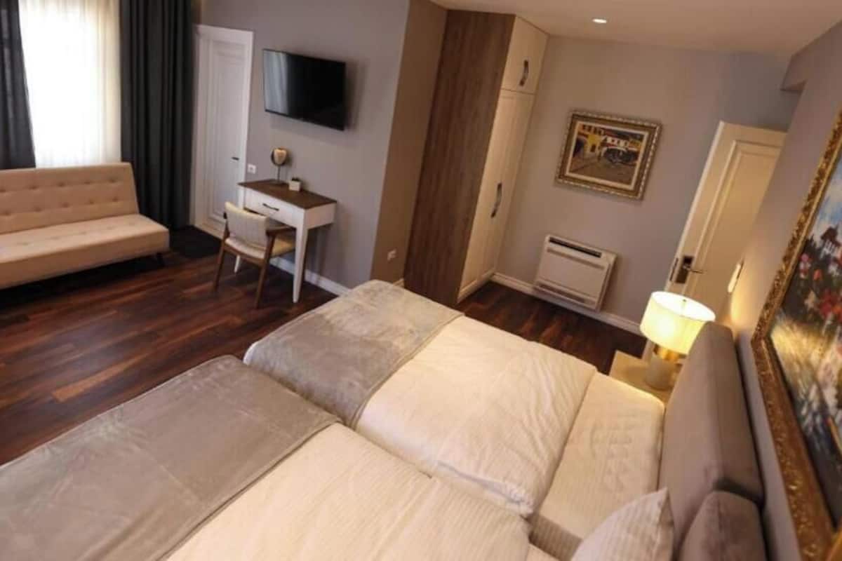 A hotel room with a bed, a sofa, a desk, a TV, a painting, and a wardrobe.