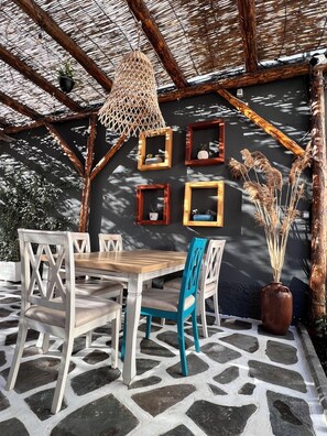 Un área de estar al aire libre con una mesa y sillas, una pared con cuadros enmarcados y una planta en maceta.