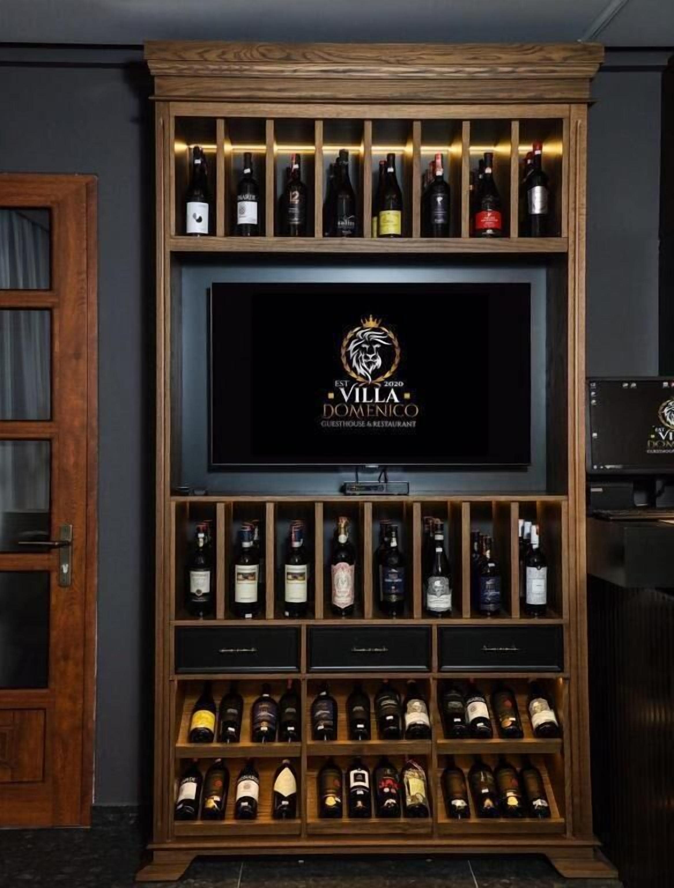 Un meuble à bouteilles contenant plusieurs bouteilles de vin, un écran de télévision avec un logo et un buffet en bois.