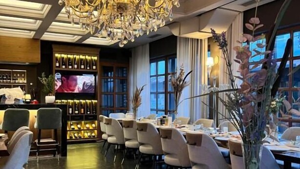 A restaurant with a chandelier, tables with chairs, a bar area, and a television screen. - Villa Domenico Korce Old Bazaar (Korçë)