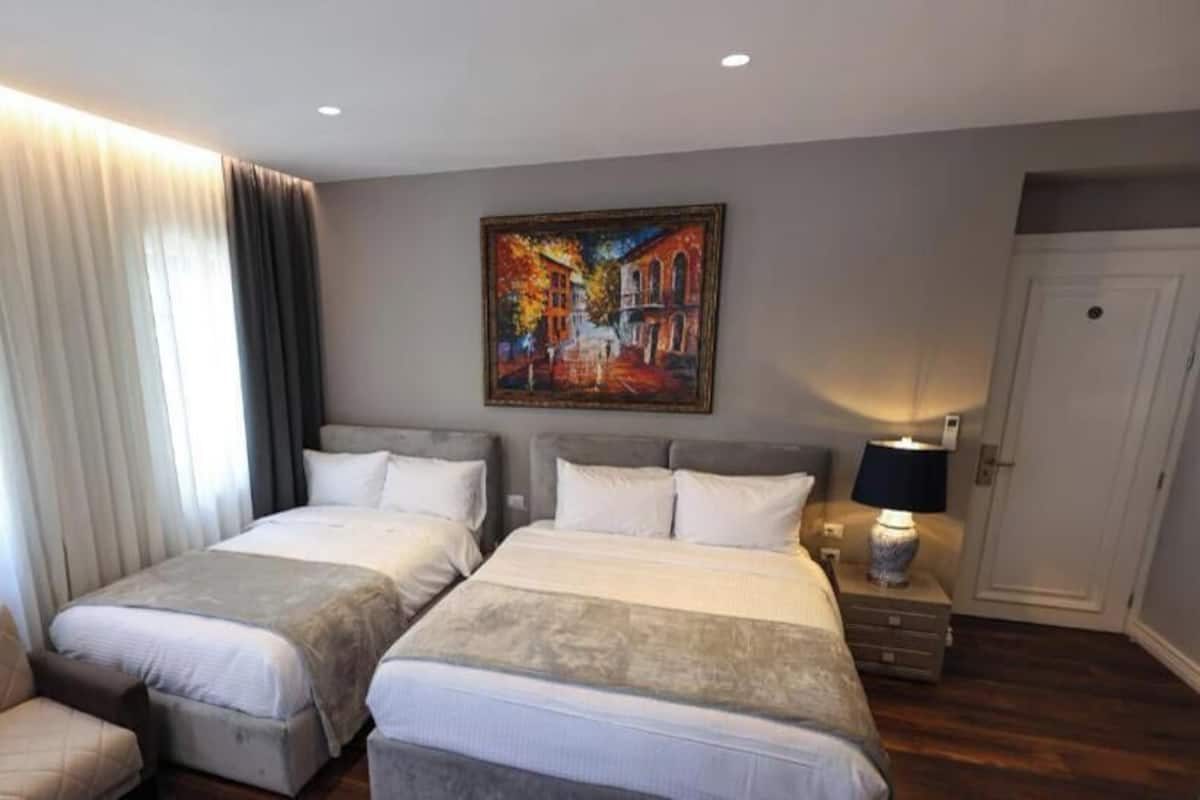 Una habitación de hotel con dos camas, una silla, un cuadro en la pared y una puerta.