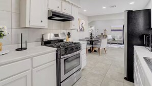 Una cucina moderna con mobili bianchi, piano cottura a gas, forno e zona pranzo con tavolo e sedie.