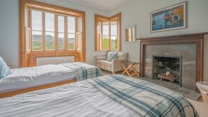 Un dormitorio con dos camas, una chimenea y ventanas amplias con vistas.