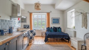 Una habitación acogedora con cama, ventana con cortinas, zona de cocina con estufa y radiador.