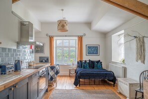 Ein gemütliches Zimmer mit Bett, einem Fenster mit Vorhängen, einer Küchenzeile mit Herd und einem Heizkörper.