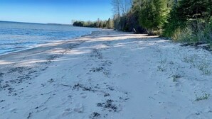 A sandy beach with a clear blue sky and trees in the background. - Sandy Toes Retreat,stunning view & just 25 steps to a sandy beach Lake Michigan. (Cedar River)