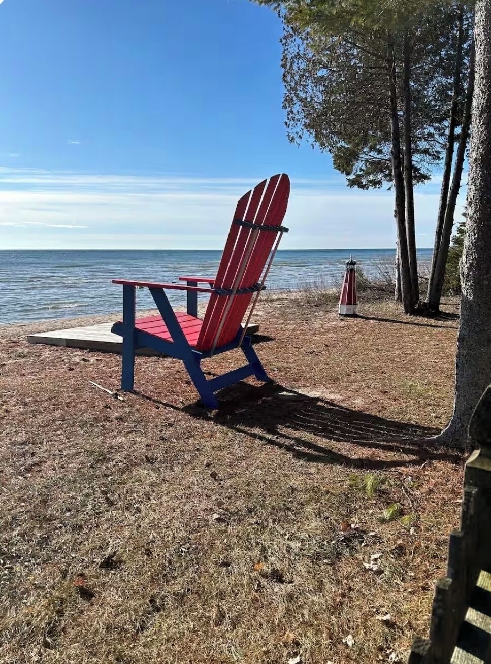 Une plage avec un fauteuil Adirondack rouge et bleu, une petite lanterne rouge et blanche et un arbre.