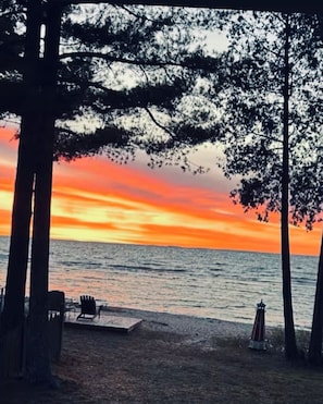 A beach scene with trees, a chair, and a small table. - Sandy Toes Retreat, pet friendly & just 25 steps to a sandy beach Lake Michigan. (Cedar River)
