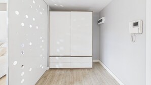 Quarto minimalista com guarda-roupa, telefone fixado na parede e chão de madeira.