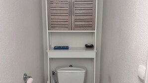 A small bathroom with a toilet, a shelf above it holding toiletries, and a toilet paper holder on the wall. - T2 Sanary near sea (Sanary-sur-Mer)