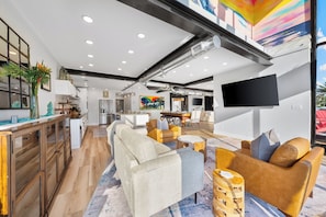 Ein modernes Interieur mit Küche, Essbereich und Wohnzimmer, mit Holzböden, einem großen Sofa und einem Flachbildfernseher.