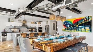 A modern kitchen with white cabinets, stainless steel appliances, and a dining area with a rustic wooden table and grey upholstered chairs. - Sleeps 10 in Jax Beach - 2BR/2BA - Pool Table + Firepit (Jacksonville Beach)