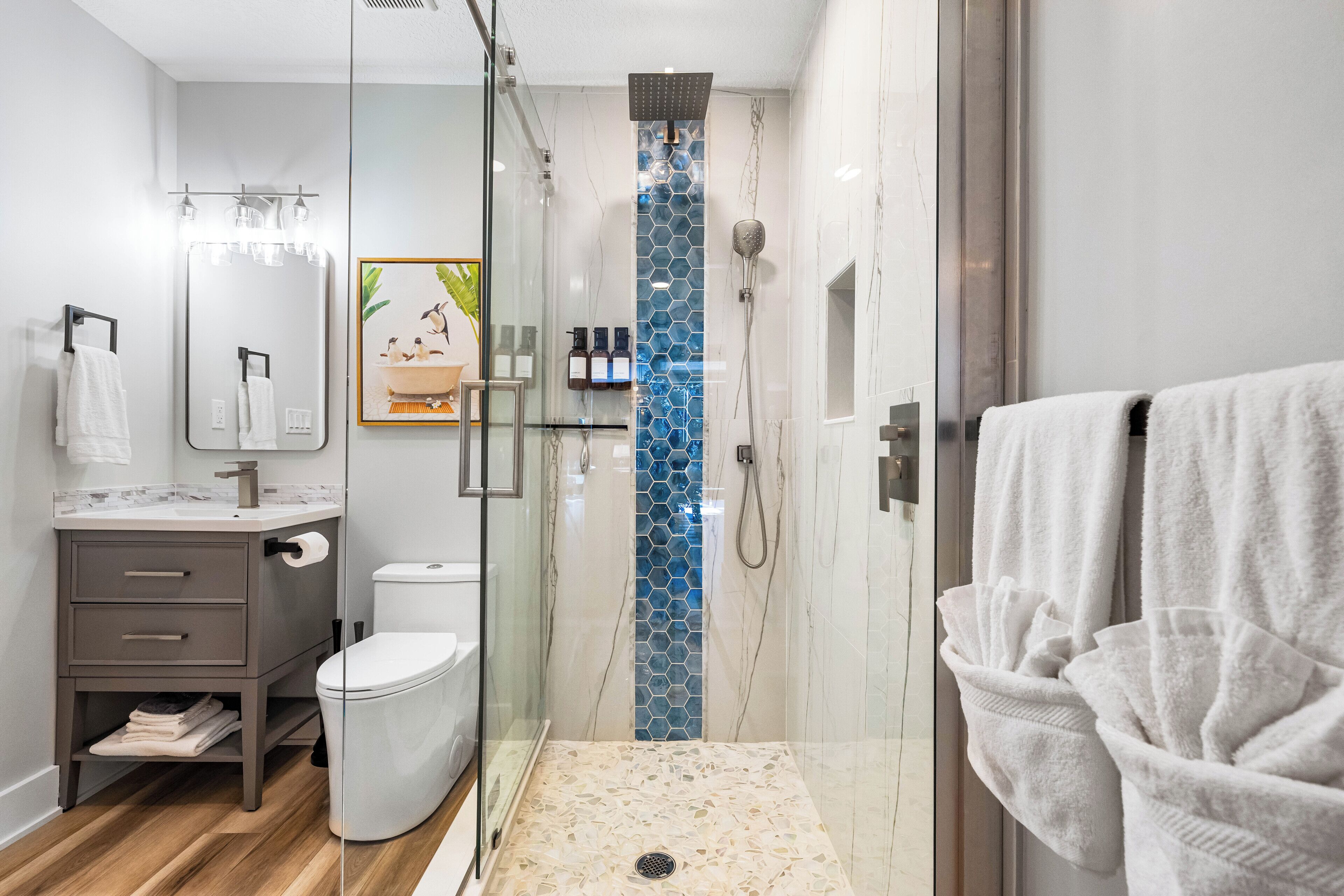 A modern bathroom with a glass shower enclosure, a toilet, a vanity with a mirror, and towels.