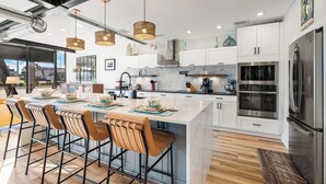 A modern kitchen with a large island, bar stools, stainless steel appliances, and pendant lighting. - Sleeps 10 in Jax Beach - 2BR/2BA - Pool Table + Firepit (Jacksonville Beach)