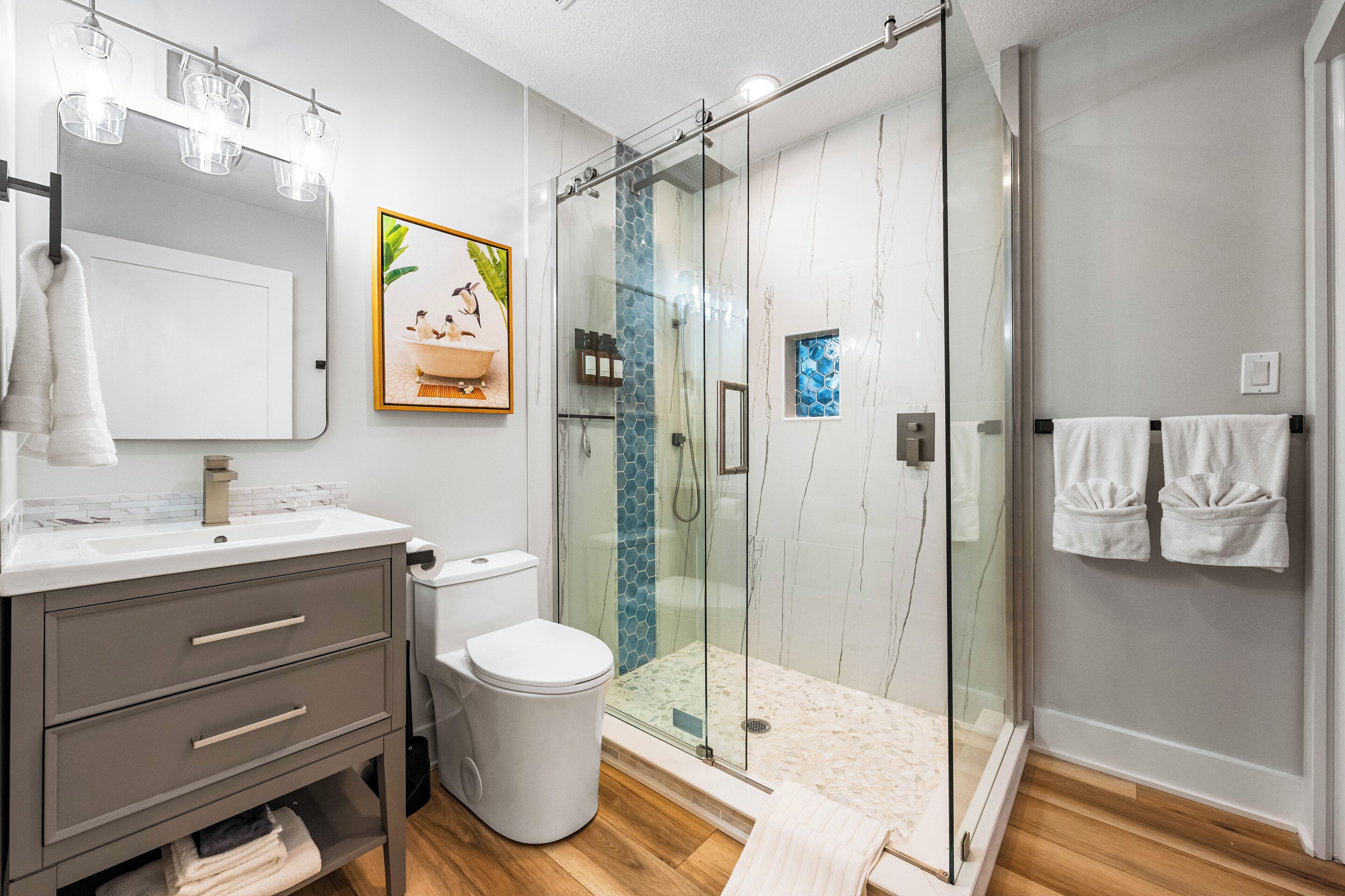 A modern bathroom with a glass shower enclosure, a white toilet, a vanity with drawers, and a mirror.