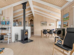 Ein gemütliches Interieur mit einem zentralen Kaminofen, einem Essbereich mit Stühlen und einem Bücherregal voller Bücher.
