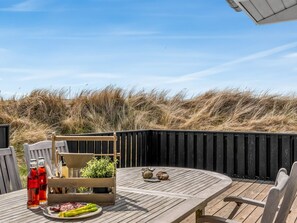 Eine Holzterrasse mit einem runden Tisch, Stühlen und einer kleinen Pflanzengruppe.