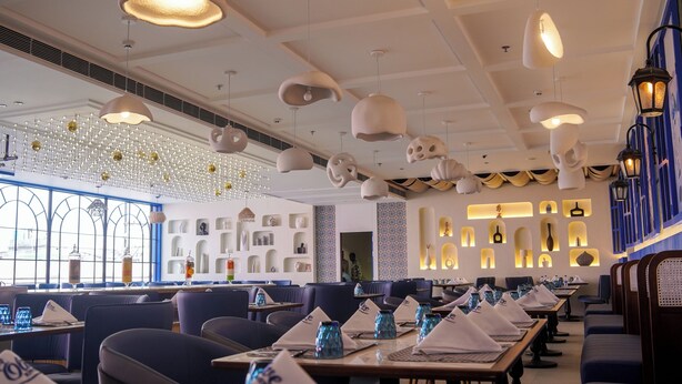 Un restaurante con mesas largas, sillas azules y luces de techo originales.