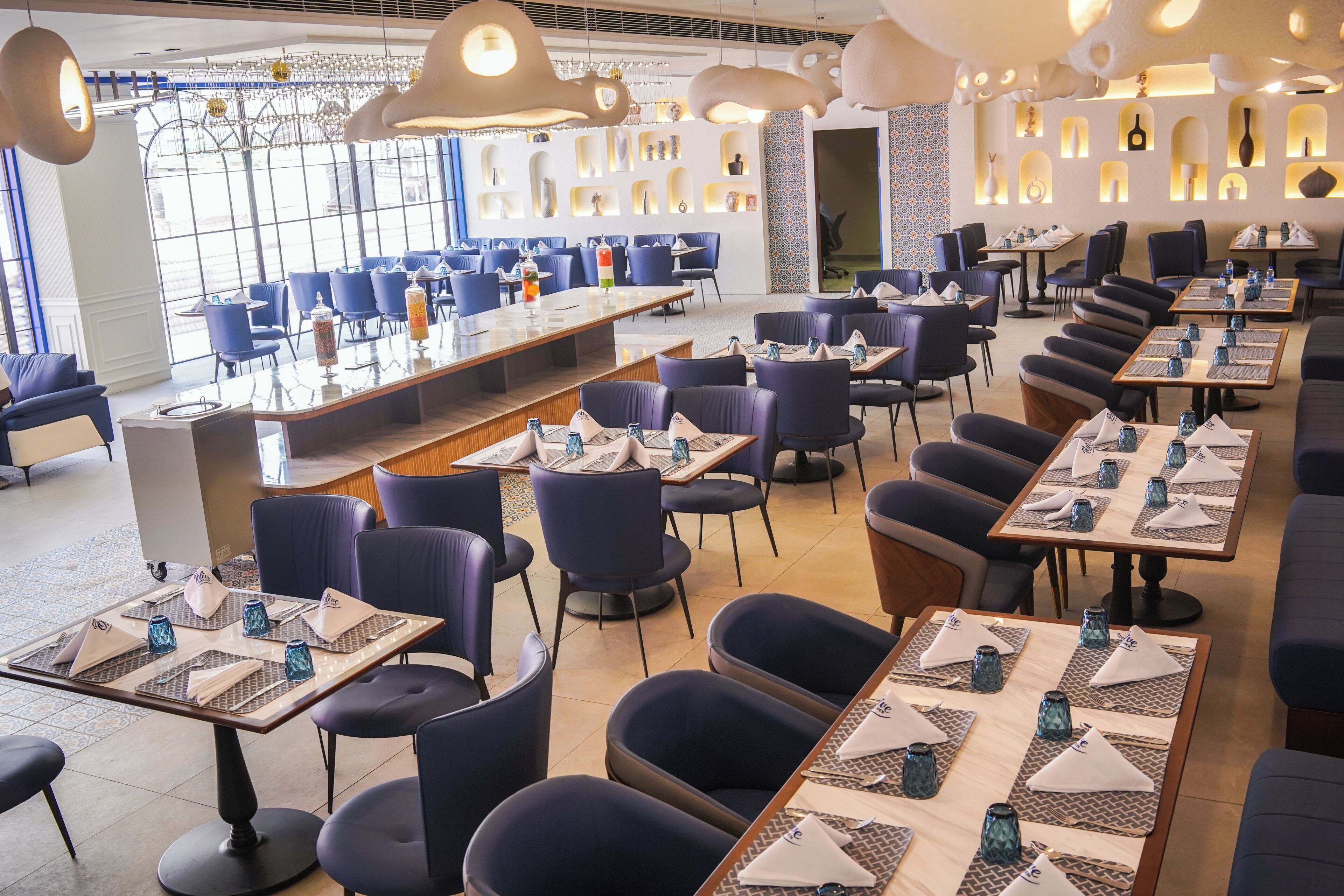 A restaurant with multiple tables and chairs, a long counter, and a view through large windows.