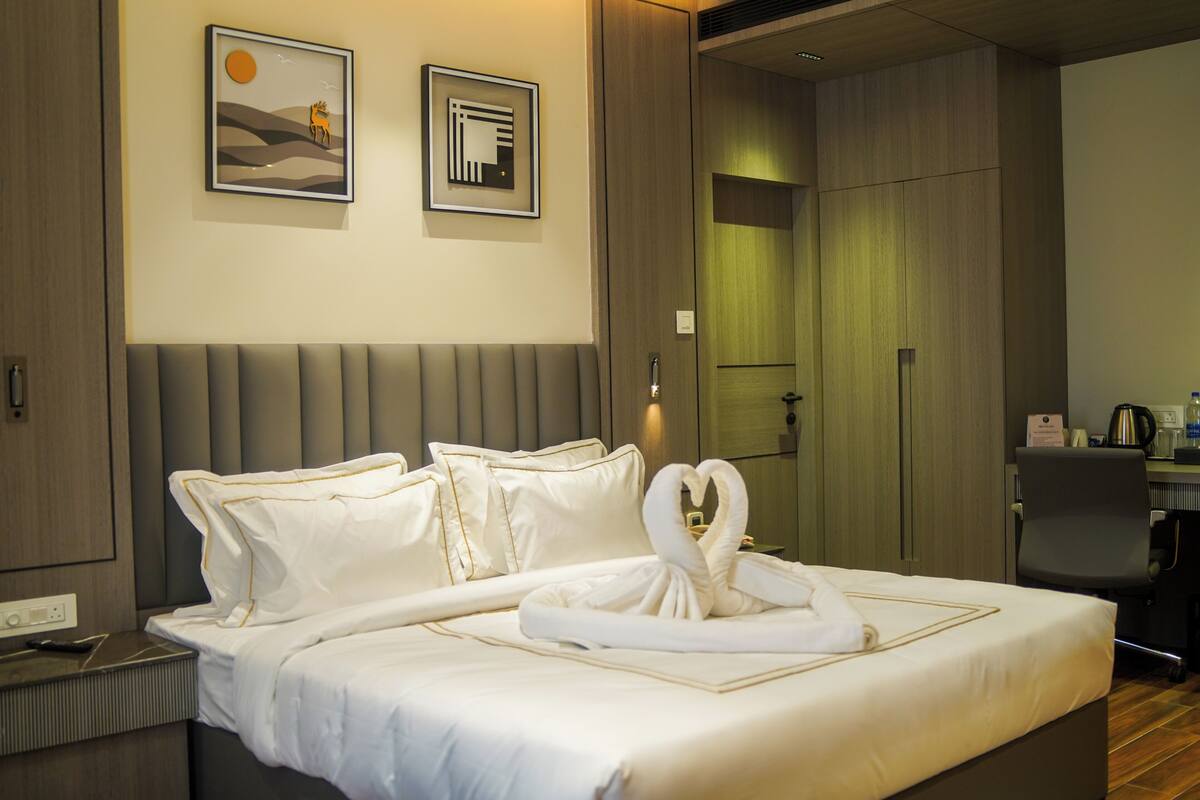 Habitación de hotel con una cama bien hecha, una mesita de noche con teléfono y cargador, y un escritorio con cafetera.