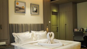 Habitación de hotel con una cama bien hecha, una mesita de noche con teléfono y cargador, y un escritorio con cafetera.