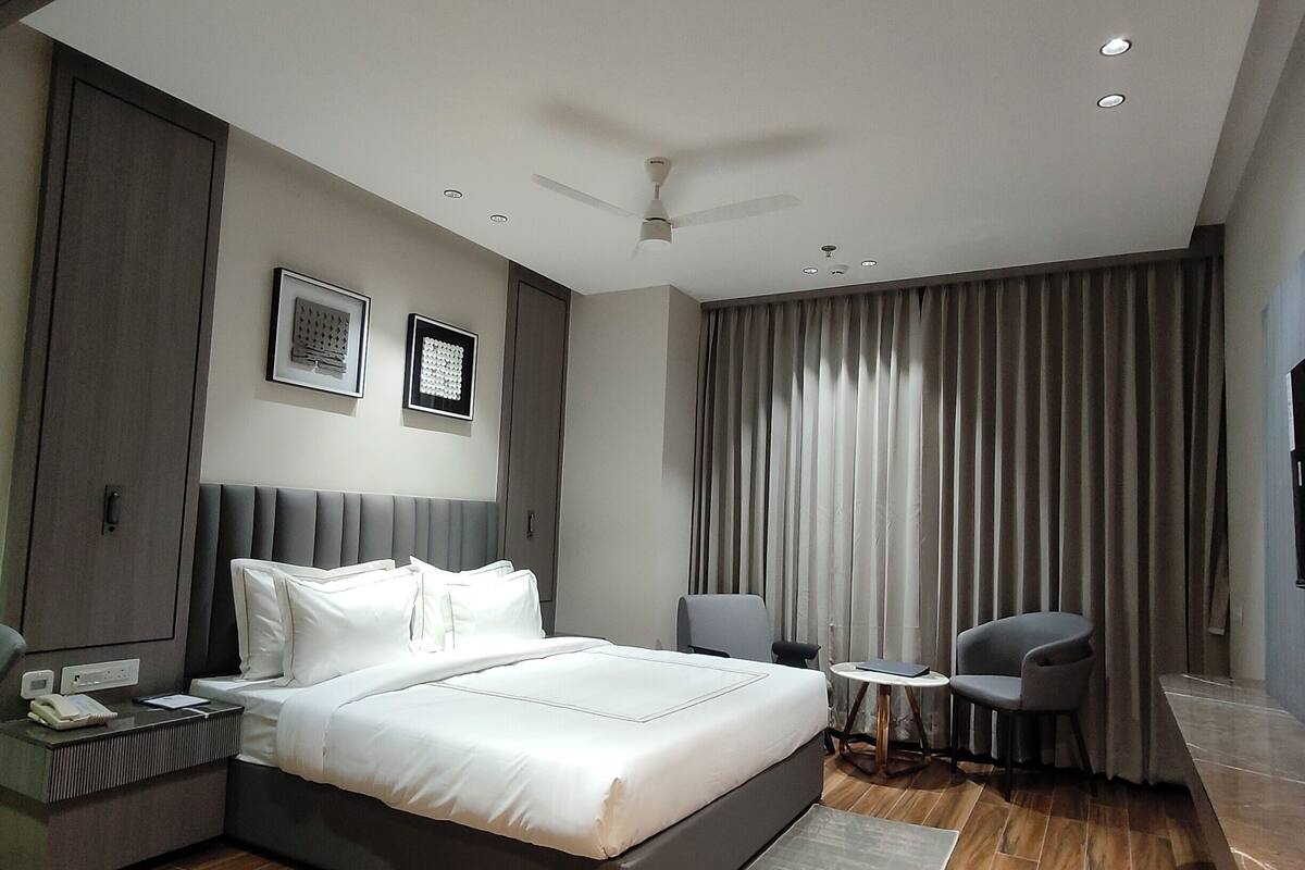 Una habitación de hotel moderna con una cama grande, un escritorio, una silla, un ventilador de techo y una ventana con cortinas.
