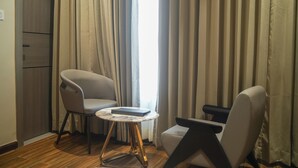 Una habitación con un armario de madera, dos sillas, una pequeña mesa redonda con un libro y un ventanal con cortinas.
