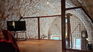 Ein Dachzimmer mit freiliegenden Steinwänden, Holzboden, Fernseher und einem großen Fenster.