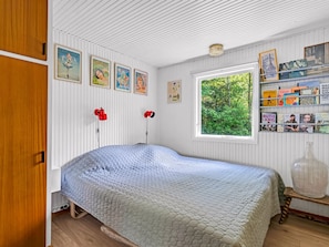 A bedroom with a bed, a window with a view of greenery, wall-mounted bookshelves, and a wooden wardrobe. - "Erk" -  from the sea by Interhome (Hadsund)