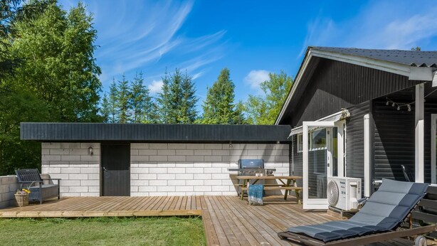 Eine moderne Außenterrasse mit Grill, Liegestühlen und einem Holztisch.