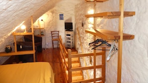 A cozy attic room with a wooden staircase, a bed, a chair, a TV, and shelves.