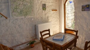A rustic room with a map, a radiator, a wooden table with chairs, a potted plant, and a stone wall.