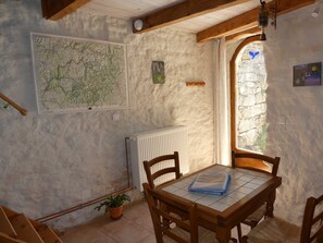 A rustic room with a map, a radiator, a wooden table with chairs, a potted plant, and a stone wall. - Le Clapas - MAS-SAINT-CHELY (MAS-SAINT-CHELY)