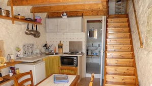 A compact kitchen with wooden cabinets, a microwave, and a sink. There's a dining table with chairs and a wooden staircase.
