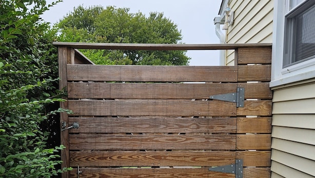 Une porte en bois, munie d’un loquet, est placée au coin d’un bâtiment dont les murs sont recouverts de bardage.