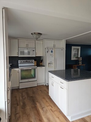 Eine Küche mit weißen Schränken, einem Doppelbackofen, einem Kühlschrank und einer Arbeitsplatte aus Granit.