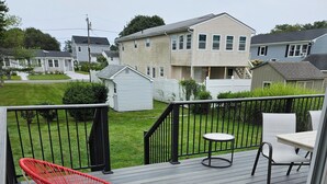 Une terrasse en bois avec deux chaises rouges et une table, le tout entouré d’une rambarde noire.